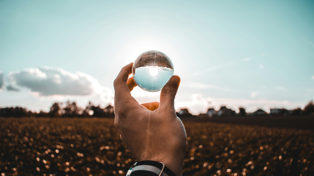 Hand holding a crystal ball over a sunny field.