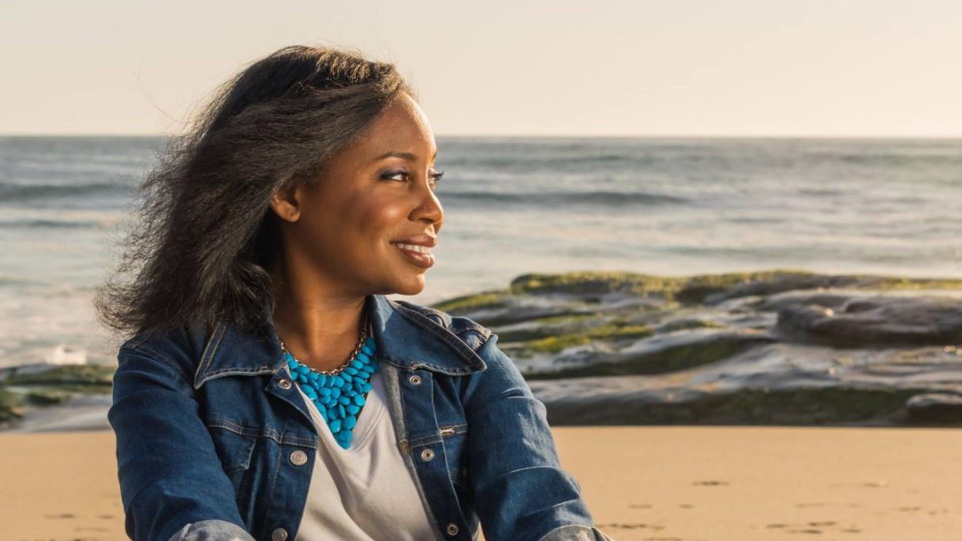 Brenda Bertrand sitting on a beach with ocean waves in the background.