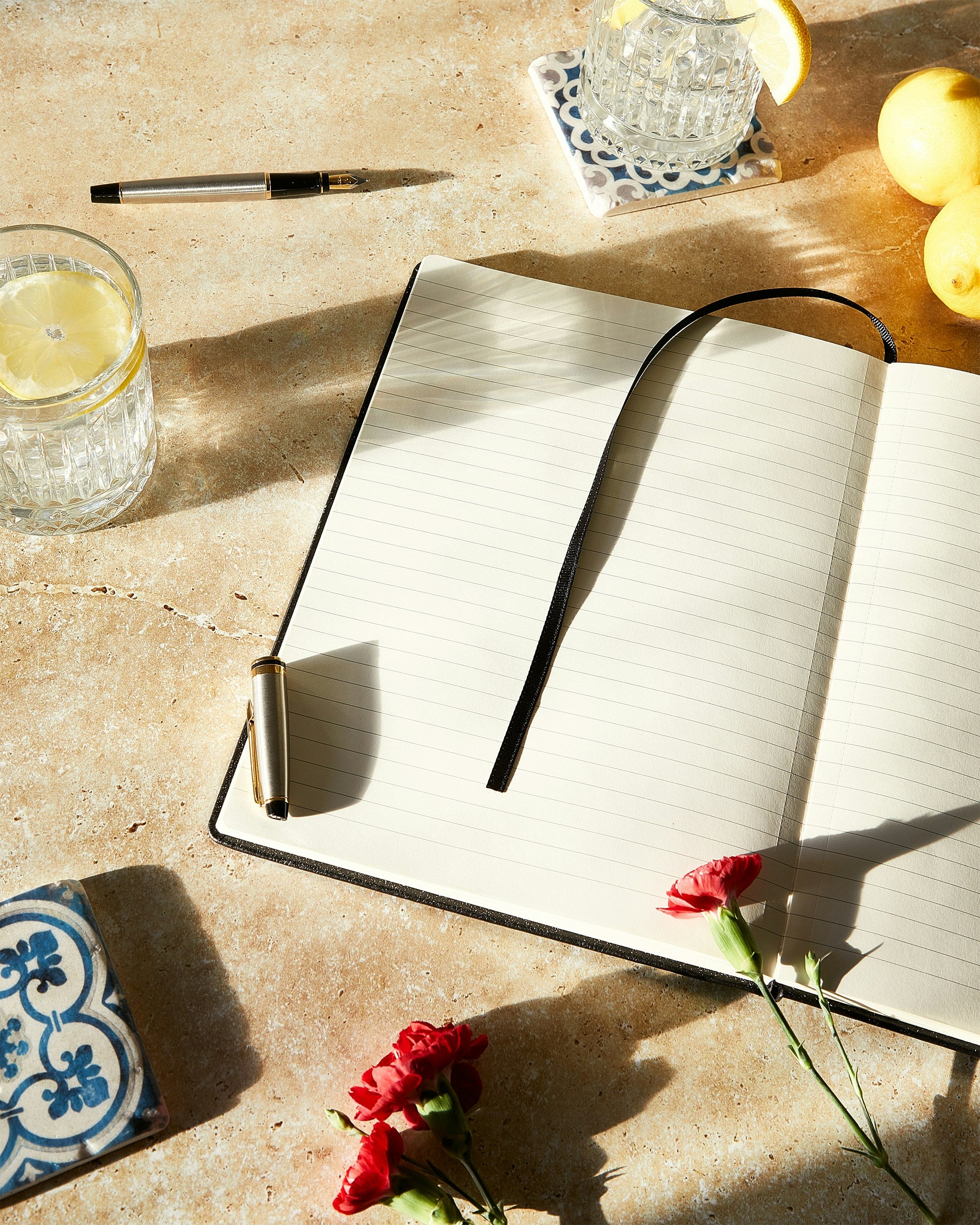 Open notebook on a textured surface with candles, flowers, and clear drinking glasses.